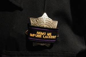 Law enforcement officers are wearing cloth labels over their badges with the words Nemo Me Impune Lacessit written across