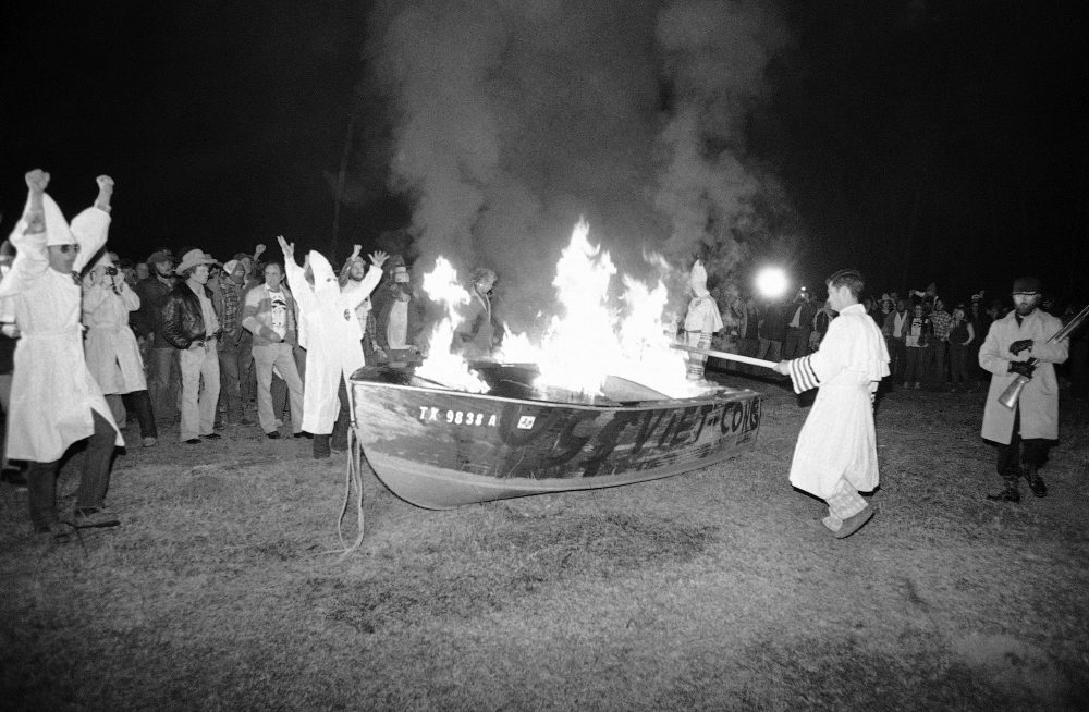 KKK members burning a small boat with the words 'Viet Cong' painted on the site