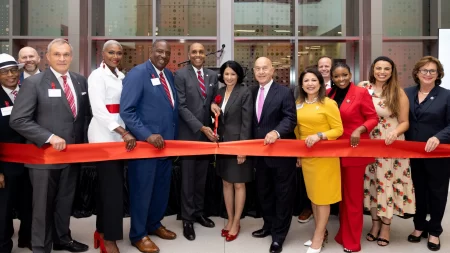 A large group of dignitaries cut a long red ribbon with oversized scissors during the grand opening of the John M O'Quinn Law Building