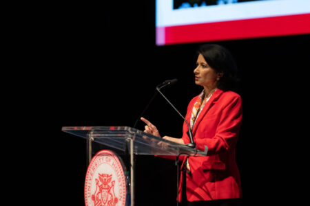 UH President Renu Khator speaks from behind a podium bearing the UH seal, wearing a red blazer