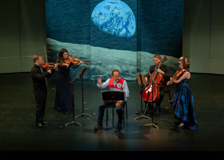 String quartet and narrator perform on stage in front of projected image